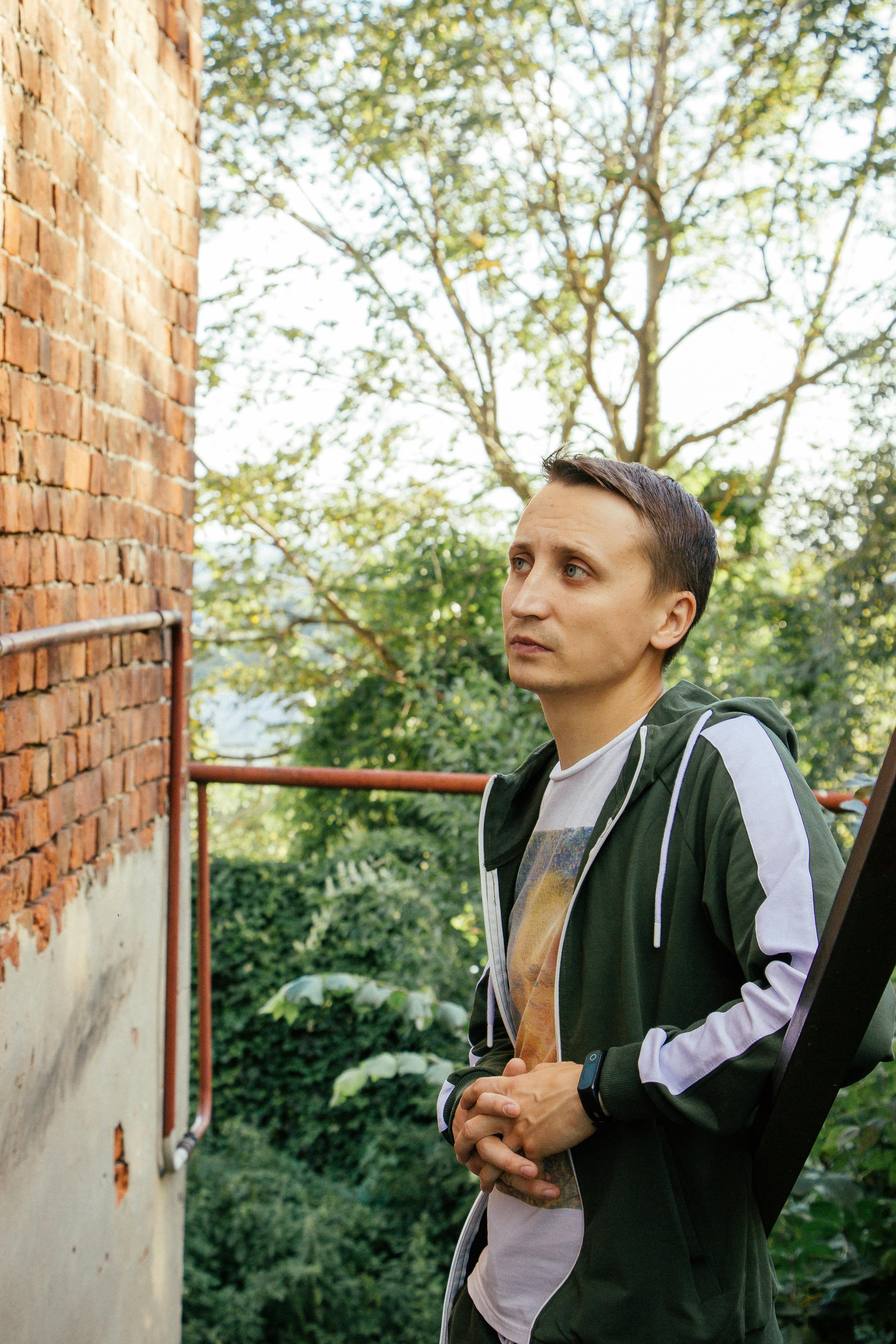 Casual portrait of a man in sportswear standing outdoors by a brick wall during summer.