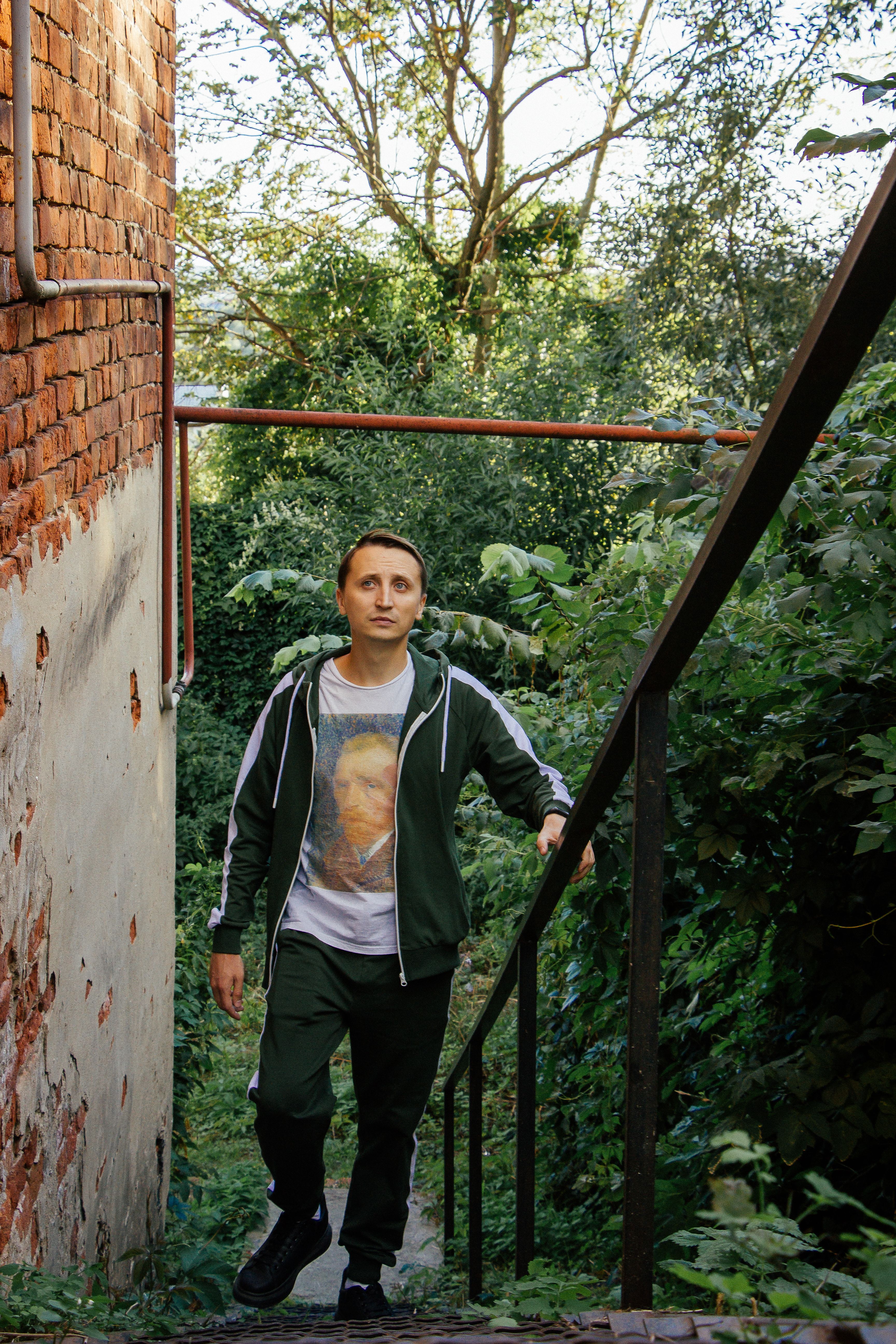 A man walks up a staircase flanked by greenery and a brick wall, capturing a serene outdoor moment.