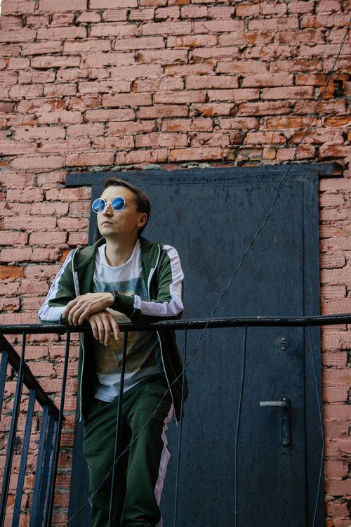 Free Fashionable man wearing sunglasses and tracksuit posing outdoors against brick wall. Stock Photo