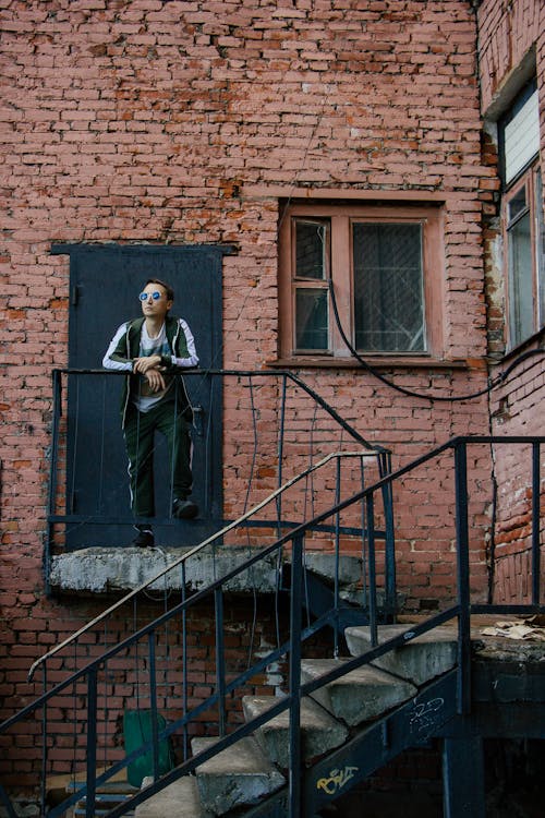 A Man Standing on the Stairs in front of a Red Brick Building 