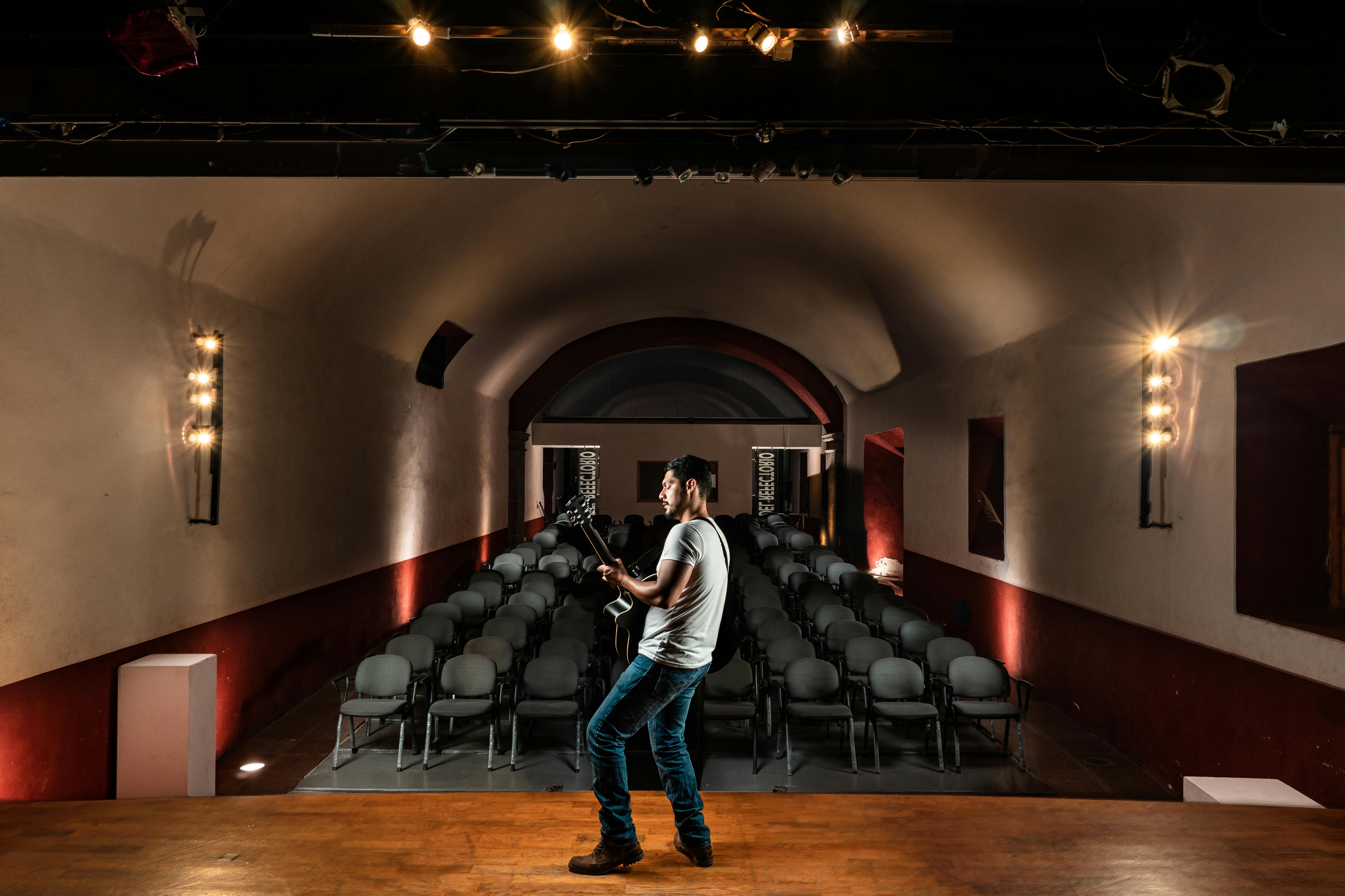 Free A lone musician playing guitar on stage in a dimly lit, empty concert hall. Stock Photo