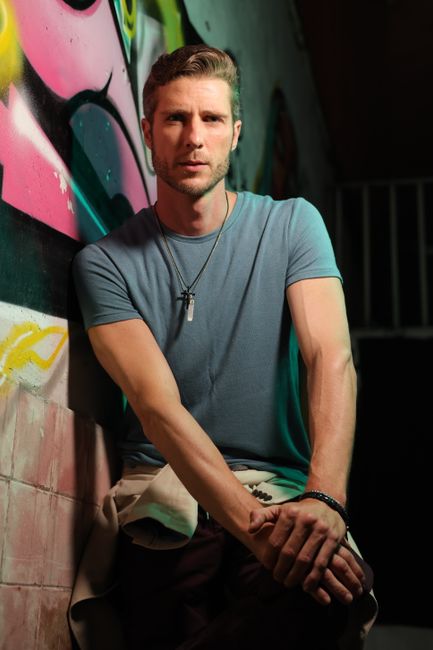Casual portrait of a man in a t-shirt leaning against a vibrant graffiti wall.