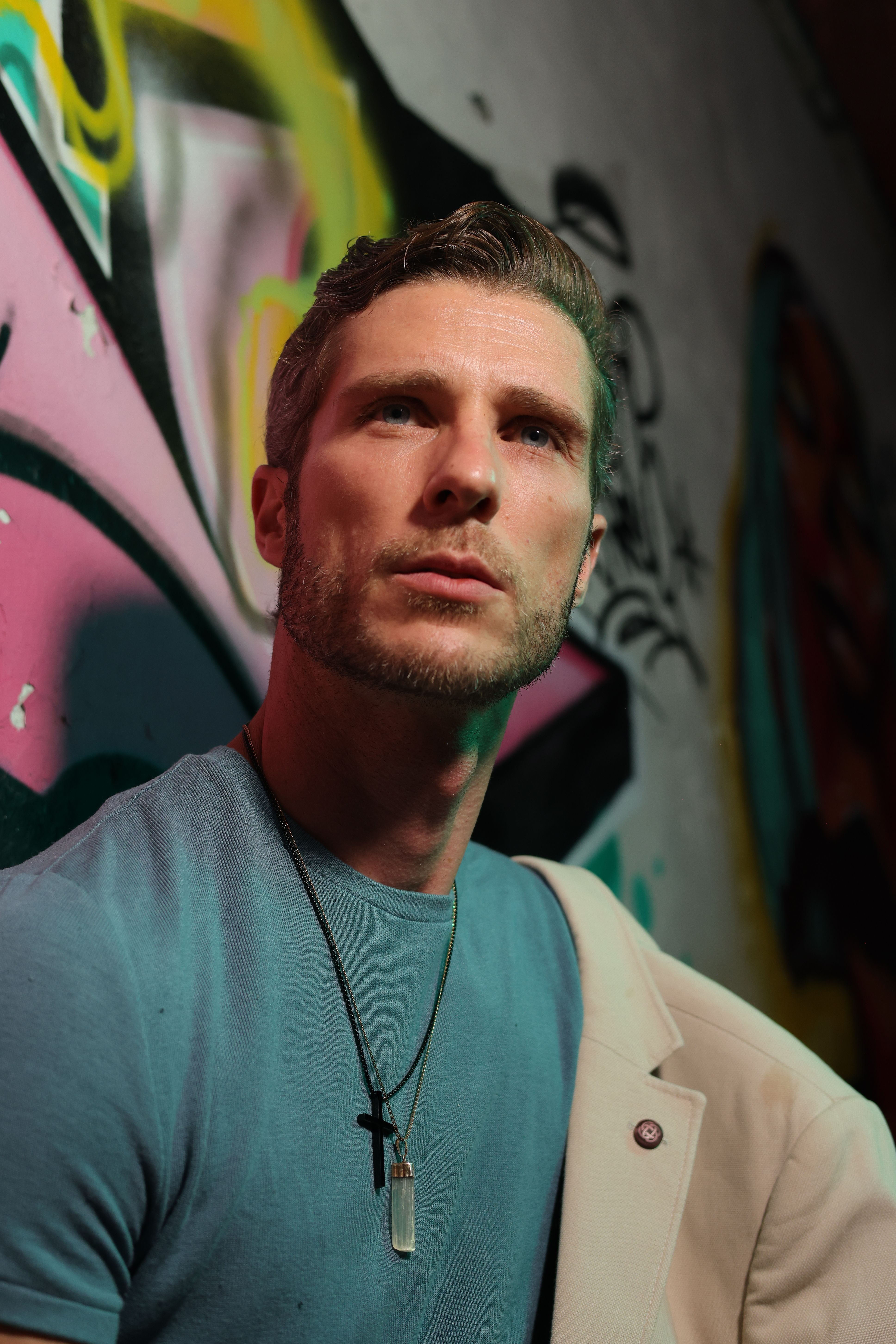 Fashionable man in blue shirt posing against colorful graffiti wall, exuding style and attitude.