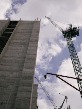 Low angle view of skyscraper under construction with cranes against blue sky.
