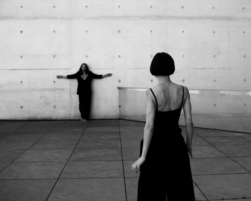 Stylish couple posing in black attire against a modern wall in Berlin, Germany.