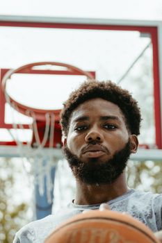 Close-up portrait of a young man holding a basketball on an outdoor court.