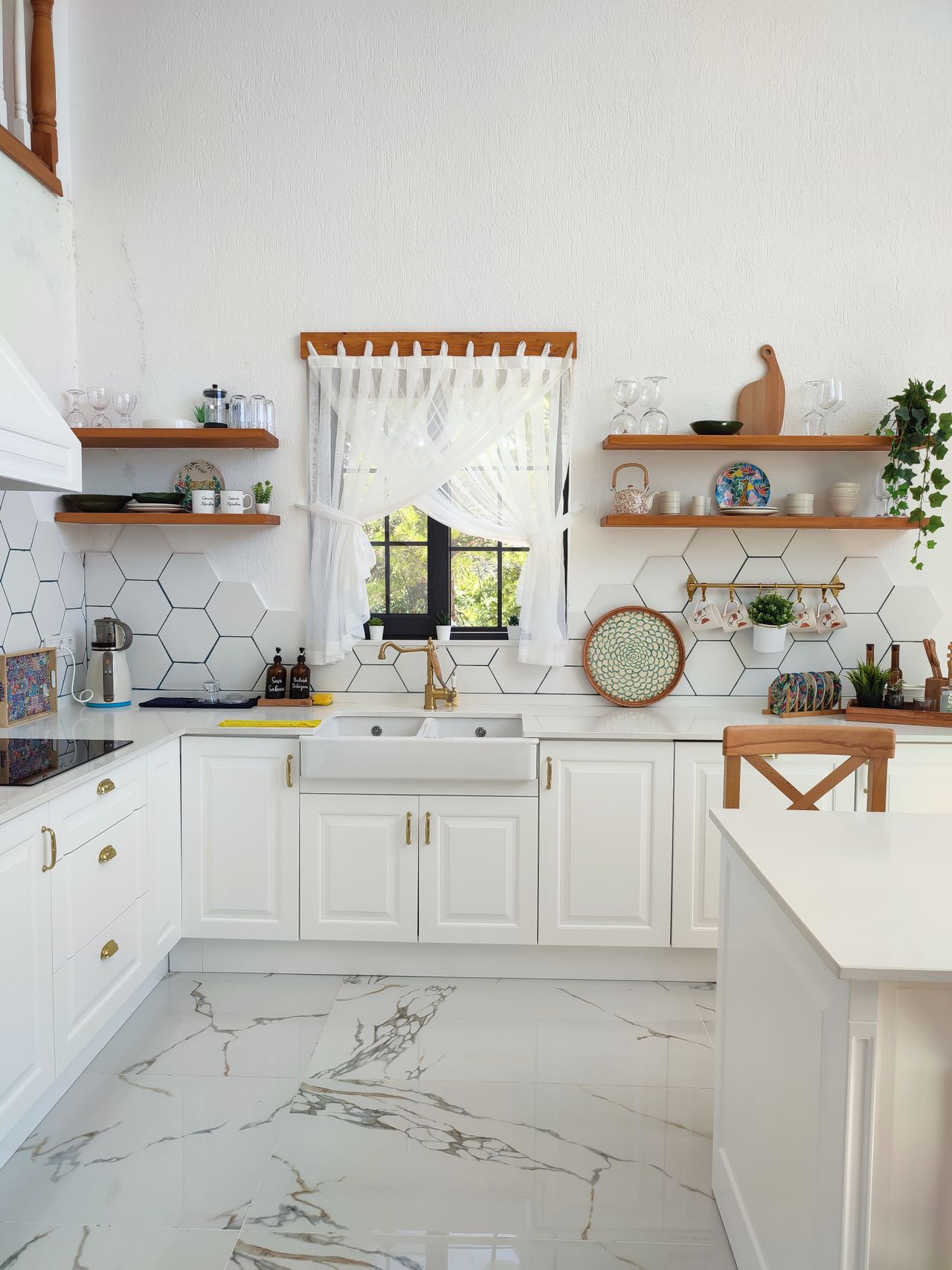Bright white kitchen with gold hardware, an apron sink, hexagon tile, and open wood shelves