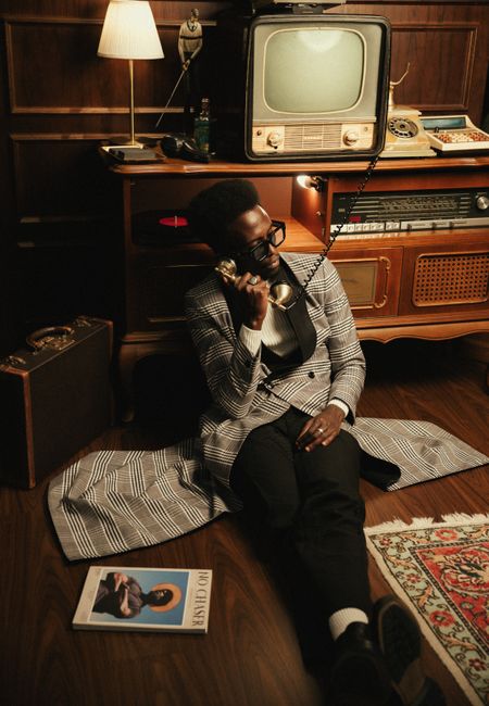 Man in vintage plaid coat using rotary phone in retro-style room with classic decor.