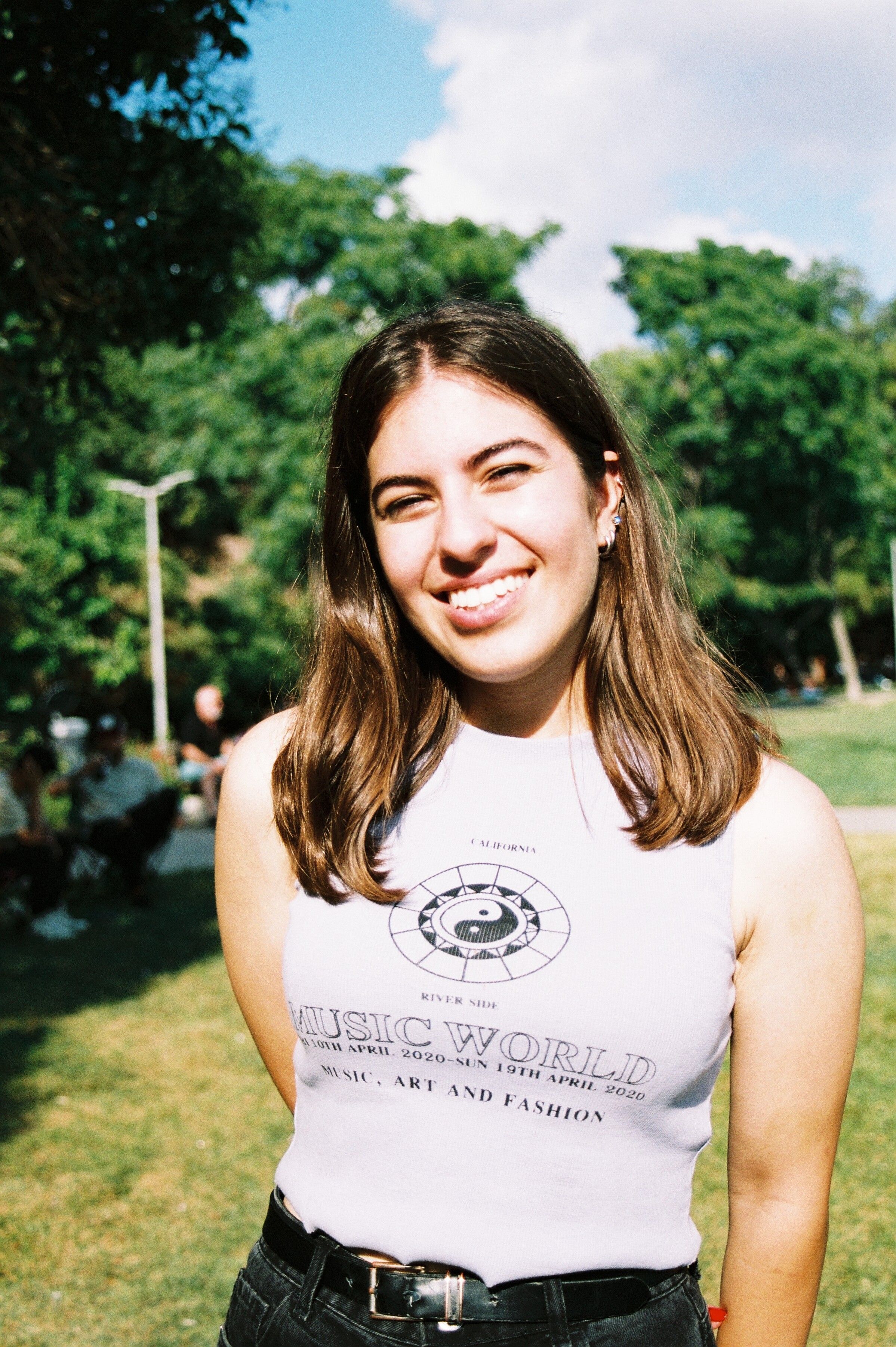Young woman smiling outdoors in a sunny park setting, capturing summer joy and leisure.