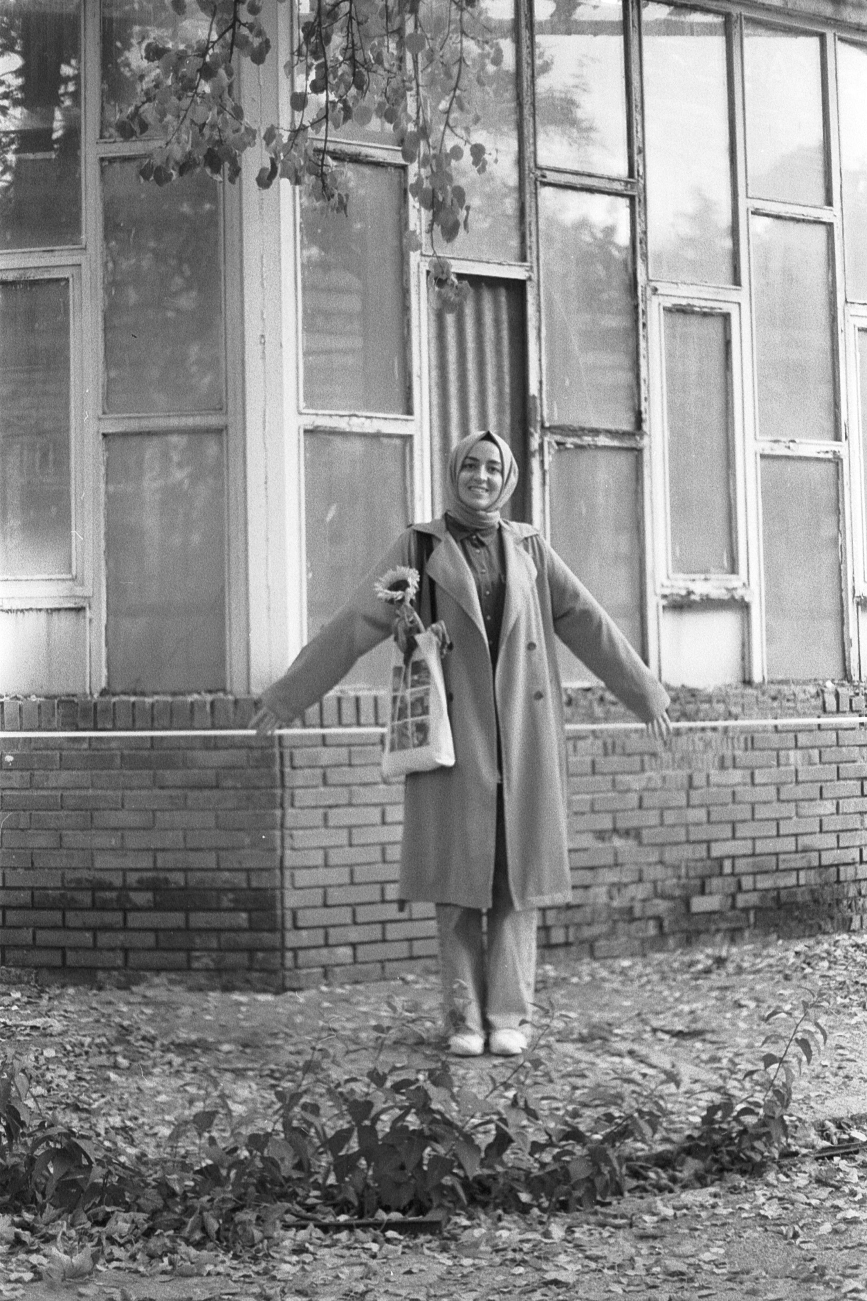 Black and white photo of a young woman in a hijab posing happily outside a building.
