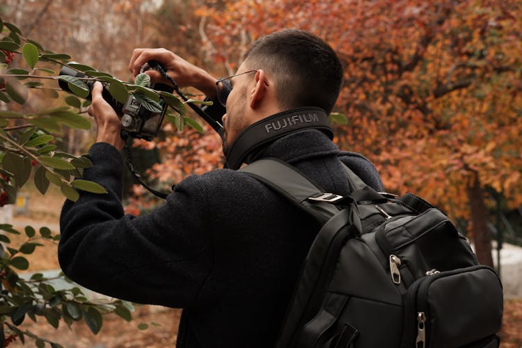 Man With Backpack Taking Pictures With Camera In Fall Forest