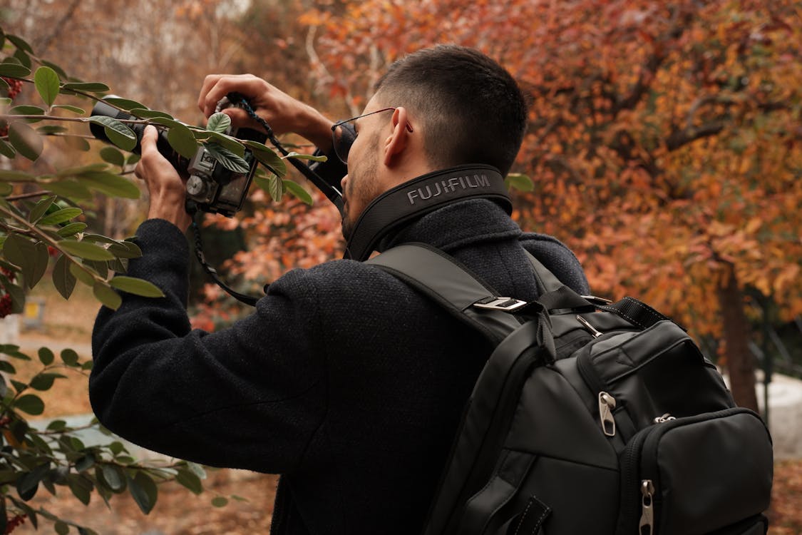 Free Man with Backpack Taking Pictures with Camera in Fall Forest Stock Photo