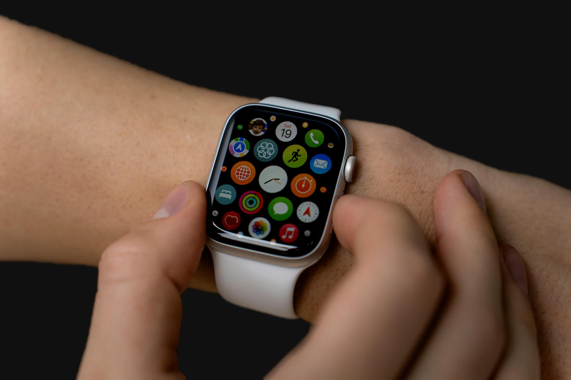 Close-up of person interacting with a smartwatch displaying apps on a dark background.