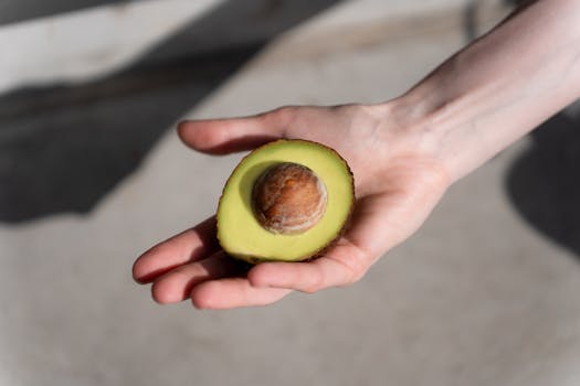 A close-up of a hand holding a ripe avocado half, highlighting its fresh and healthy appeal.