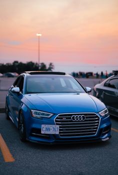 A sleek blue luxury car parked in a lot during a stunning sunset.