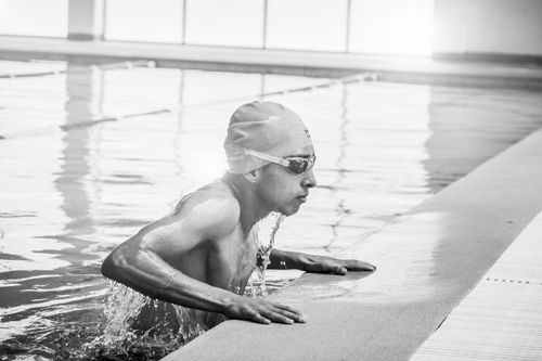 Free Athlete in swim cap and goggles rises from water in a swimming pool. Action captured in black and white. Stock Photo