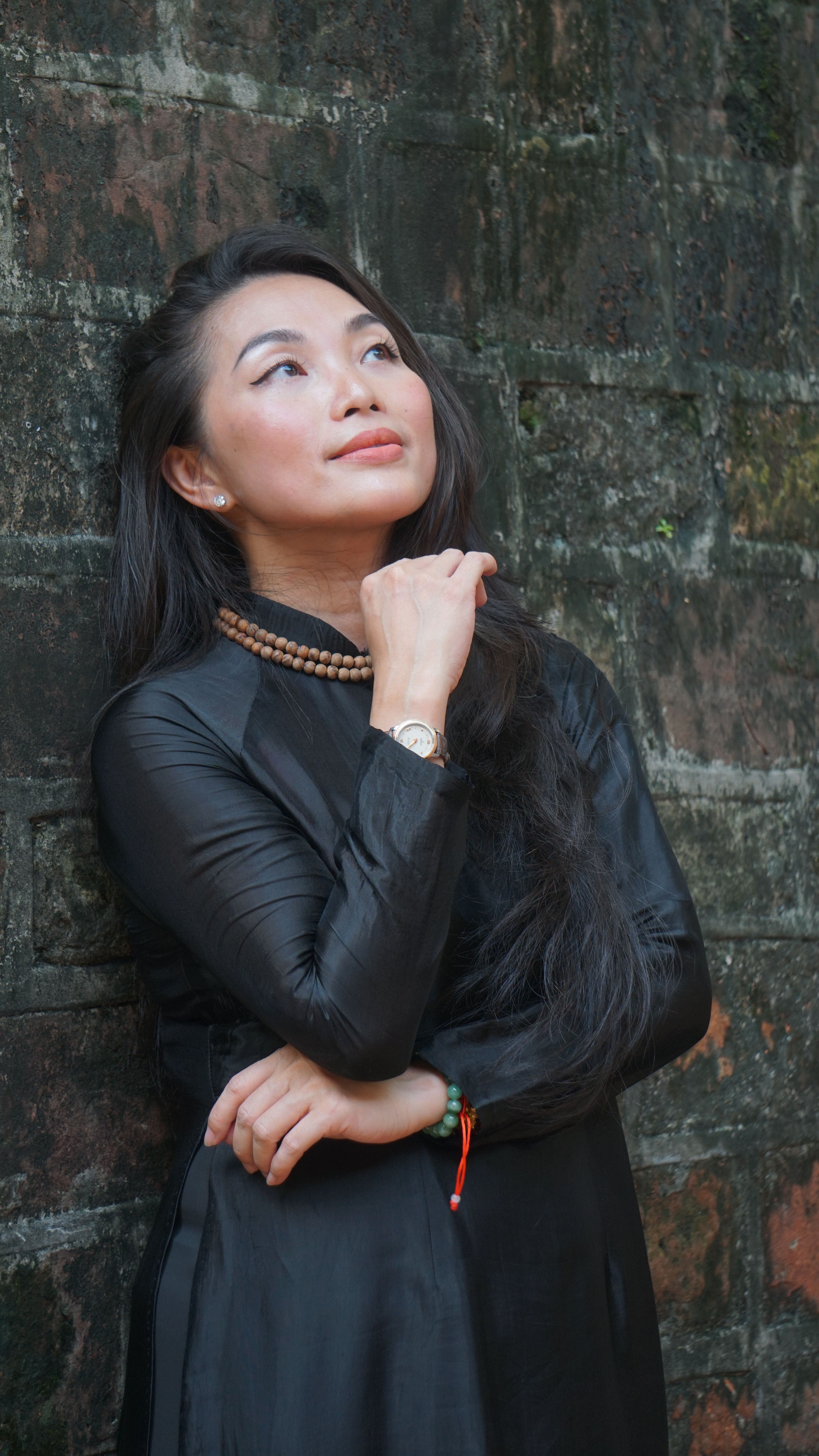 Stylish woman in a black dress gracefully posing against a rustic wall, exuding elegance.
