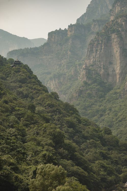 Free Stunning aerial view of a lush green mountain valley with dense forest and rocky cliffs. Stock Photo