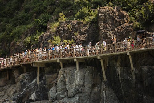 People Walking on a Wooden Trail on a Rocky Cliff 