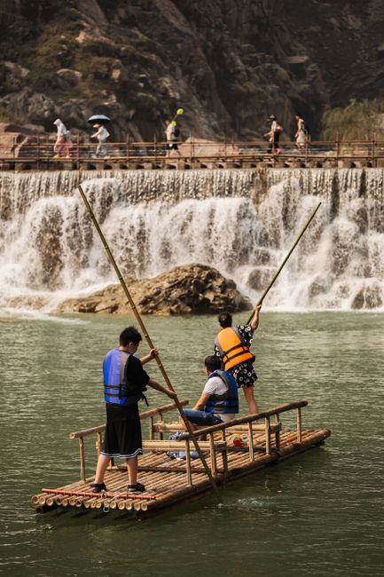 People enjoying rafting on a bamboo raft near a picturesque waterfall.