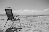 A relaxing monochrome scene of an empty chair on the sandy beach at Surfers Paradise, Australia.