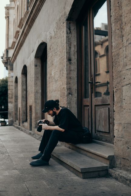 Man sitting on city steps holding a camera, captured in urban Baku setting. Daytime photo.