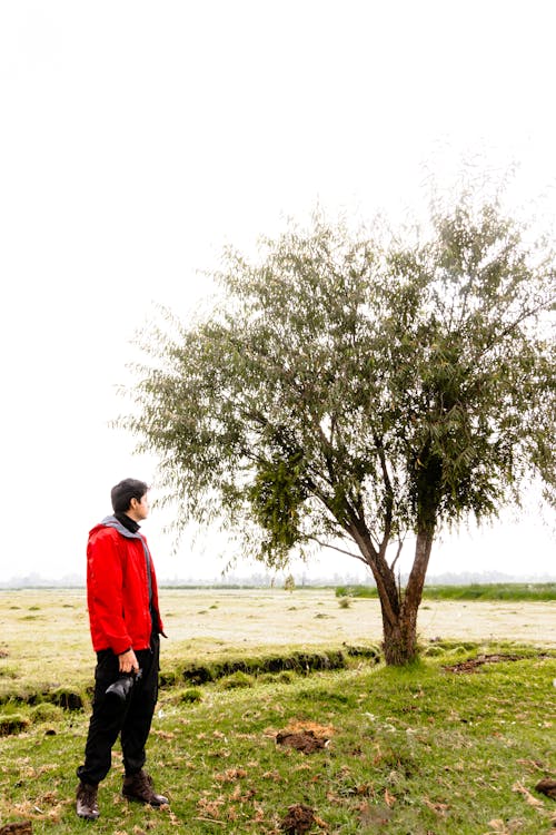 Man Holding a Camera Next to a Tree on a Field 