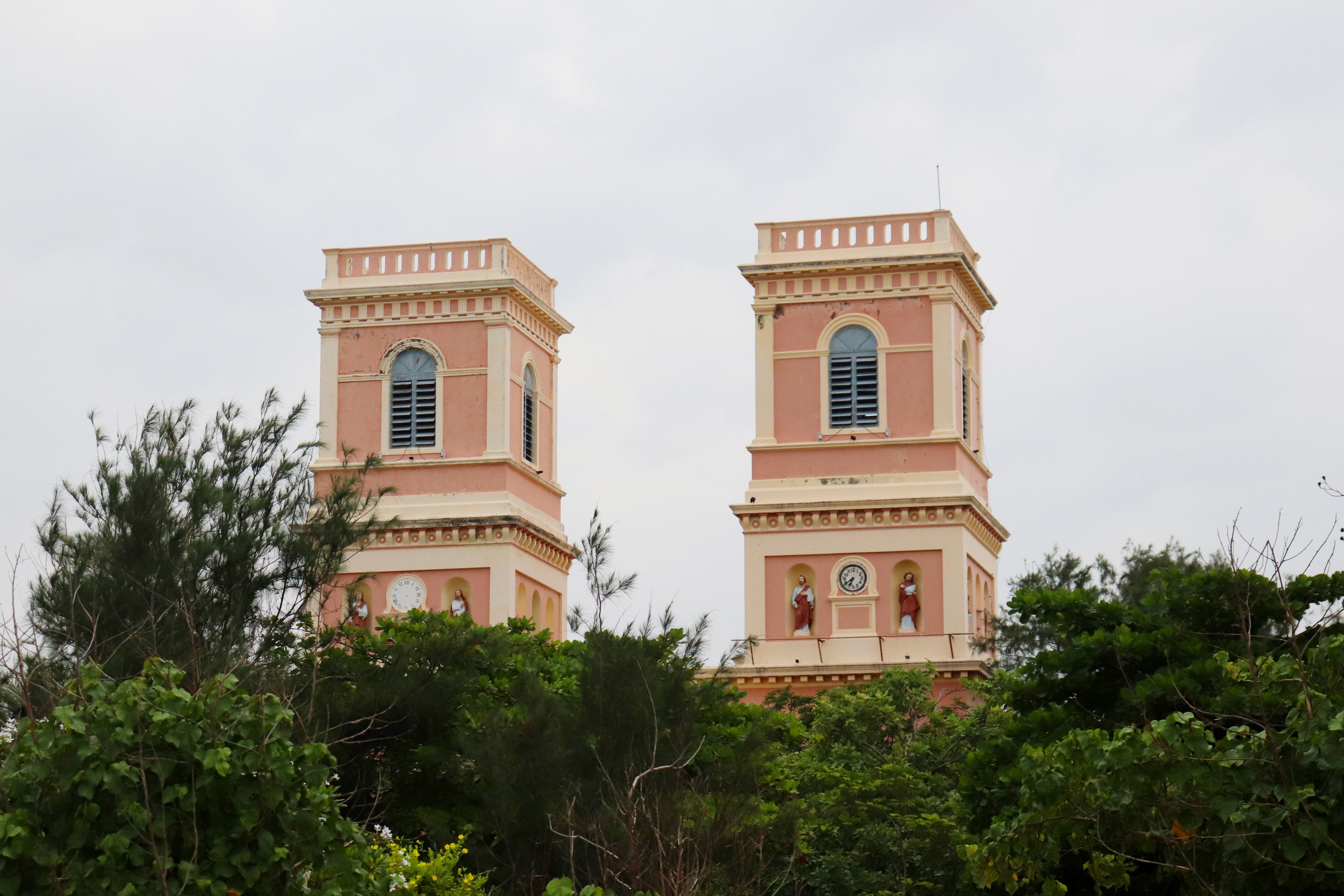 Twin towers of the Eglise de Notre Dame des Anges in Pondicherry, framed by lush greenery.