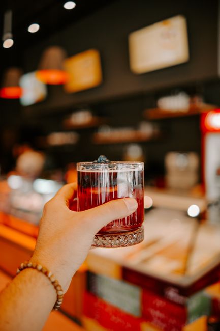 A person holds a glass of red berry drink in a cafe setting, showcasing detail and warmth.