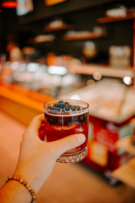 Hand holding a blueberry-infused drink in a cozy café, capturing a vibrant atmosphere.