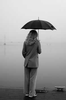 A woman stands on a wooden dock holding an umbrella, overlooking a foggy shoreline in Jönköping, Sweden.