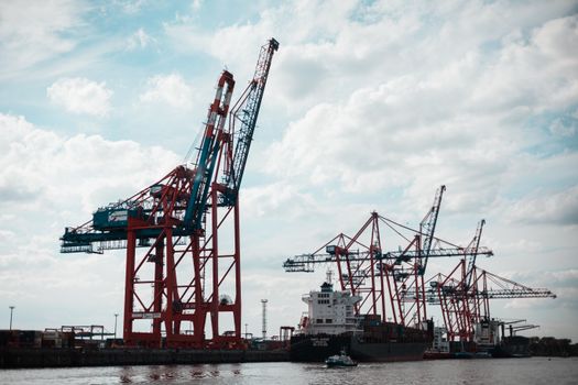 Industrial scene with container cranes at Hamburg port under a cloudy sky.