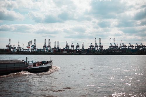 Free A cargo ship sails past cranes at Hamburg's busy container port under a cloudy sky. Stock Photo
