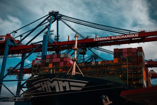 Large cargo ship docked at Terminal Burchardkai in Hamburg with containers and cranes.