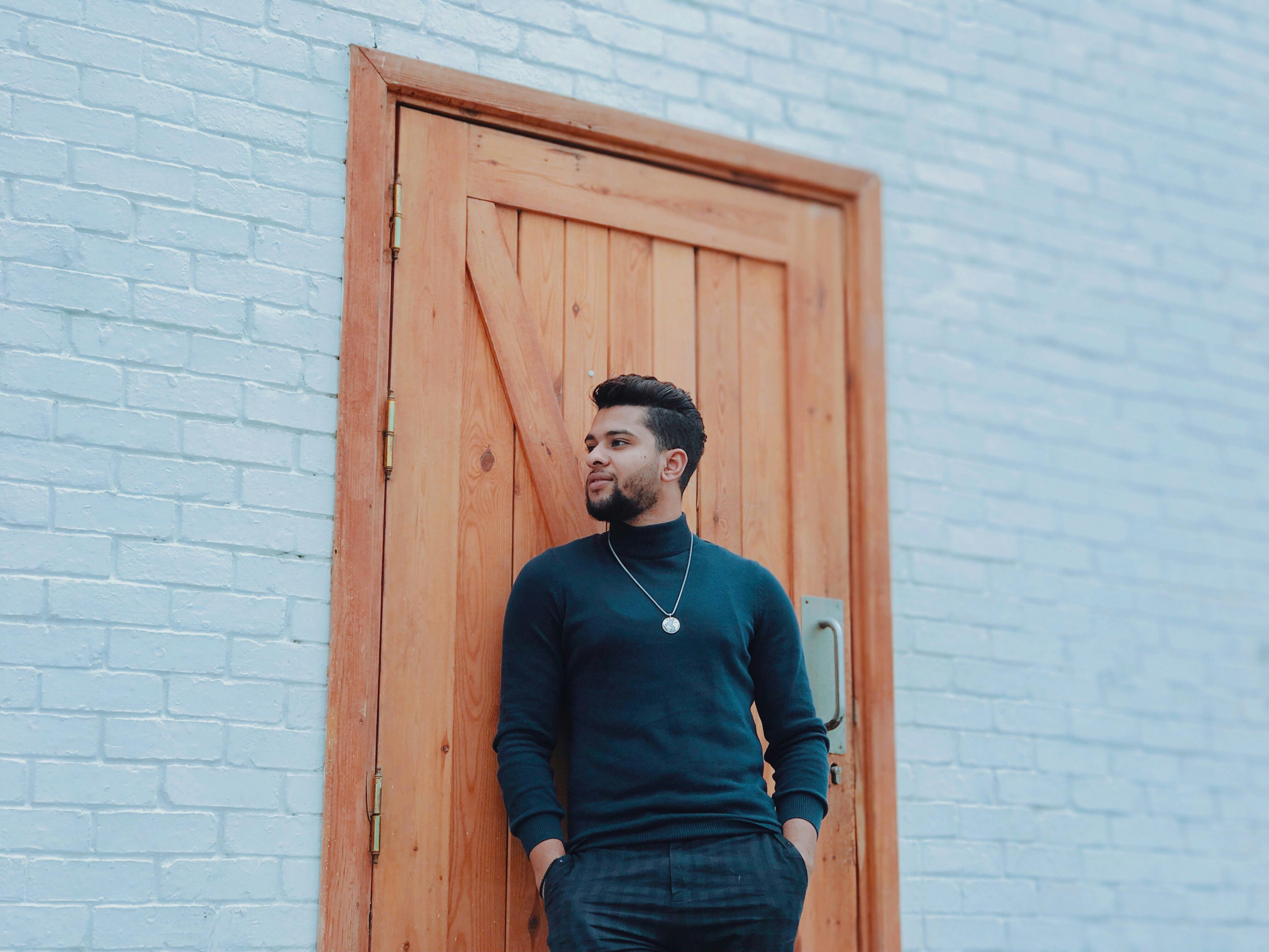 一名男子随意靠在砖墙的木门上