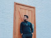 一名男子随意靠在砖墙的木门上