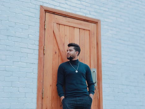 Casual portrait of a man leaning against a wooden door set in a brick wall.