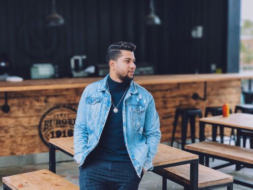 Free Young man in denim jacket relaxing at an outdoor restaurant, exuding confidence and style. Stock Photo