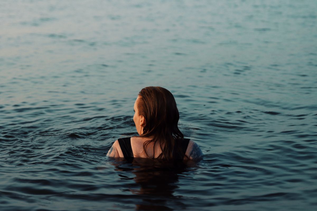 A woman swimming out into cold, still water under a grey sky