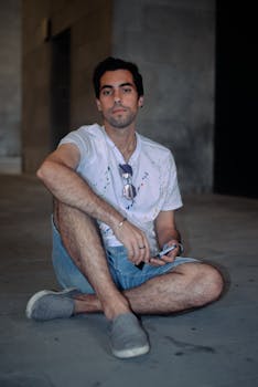 Young man in casual attire sitting in a modern Italian urban setting.