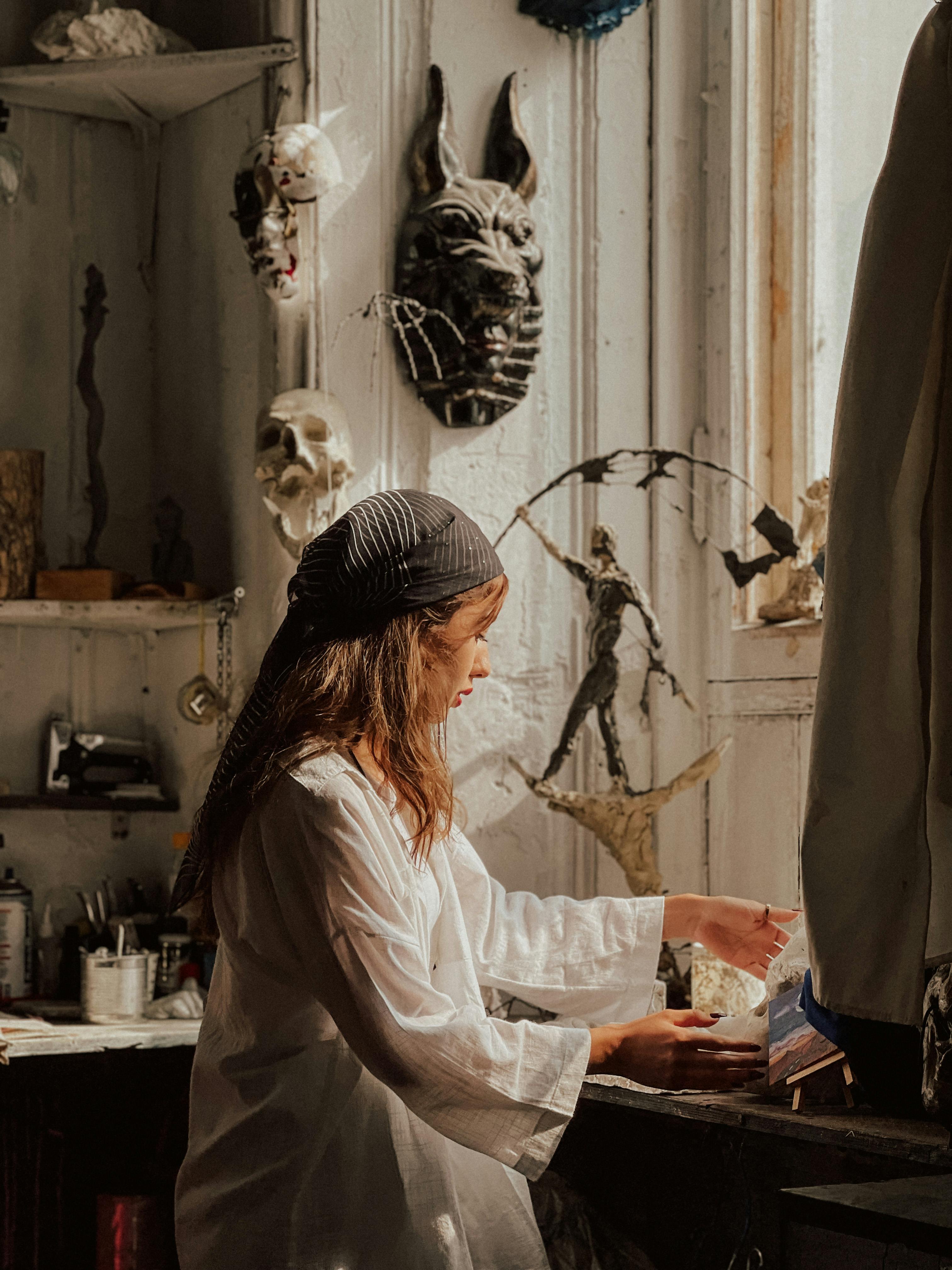 A woman artist working in a sunlit studio filled with sculptures and artistic tools.