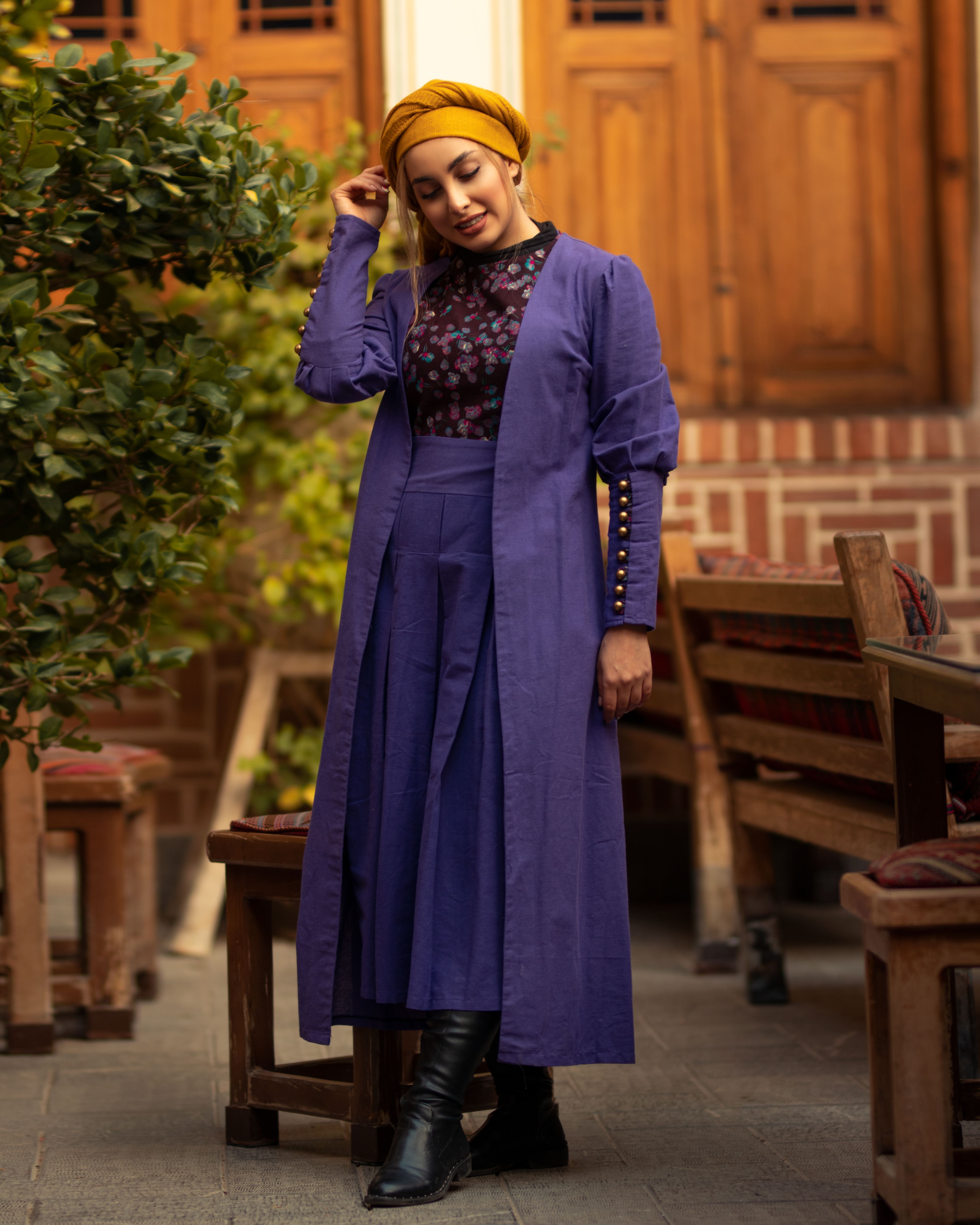 A fashionable woman in purple attire poses outdoors in Isfahan, Iran.
