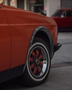 A close-up shot of a vintage custom red car's wheel in an urban setting, showcasing a polished finish.
