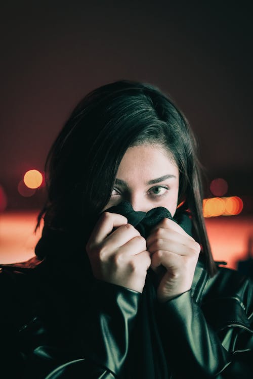 Young Woman in a Leather Jacket Standing Outside and Covering Half of Her Face with Fabric 