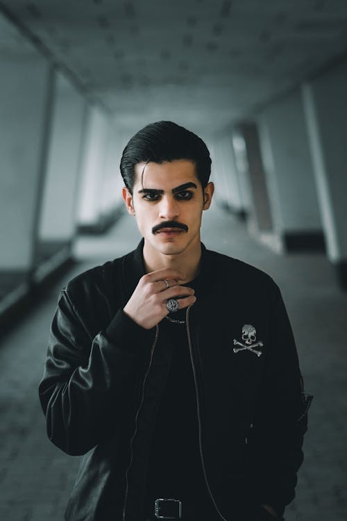 Young Man with Mustache and All Black Outfit Standing in a Hallway 