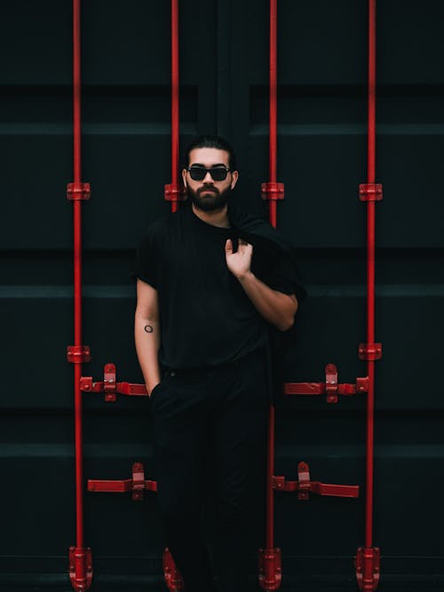 A Bearded Man with Sunglasses Standing against a Dark Wall 