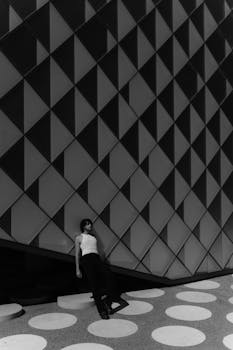 A man poses against a modern geometric-patterned wall, exuding style and fashion.