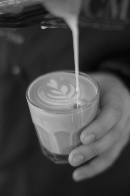 Black and white close-up of latte art being poured into a coffee cup, showcasing precision and craft.