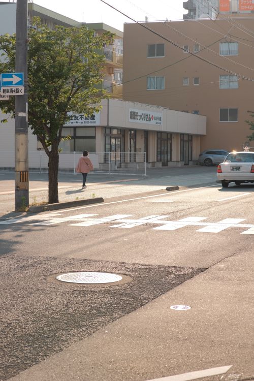Free A pedestrian crossing an urban street during daylight with cars and buildings in view. Stock Photo