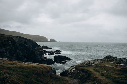 View of rugged cliffs and ocean waves at Dunlough Bay, Ireland, under a cloudy sky.